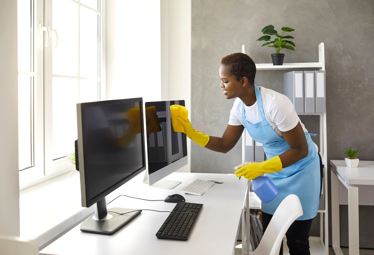 Happy Woman from Janitorial Cleaning Service Wiping Computer Screens in Modern Office